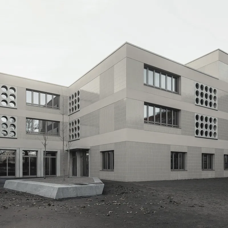 Corner view of the pale brick facade with circular perforated window panels and concrete planter in the courtyard