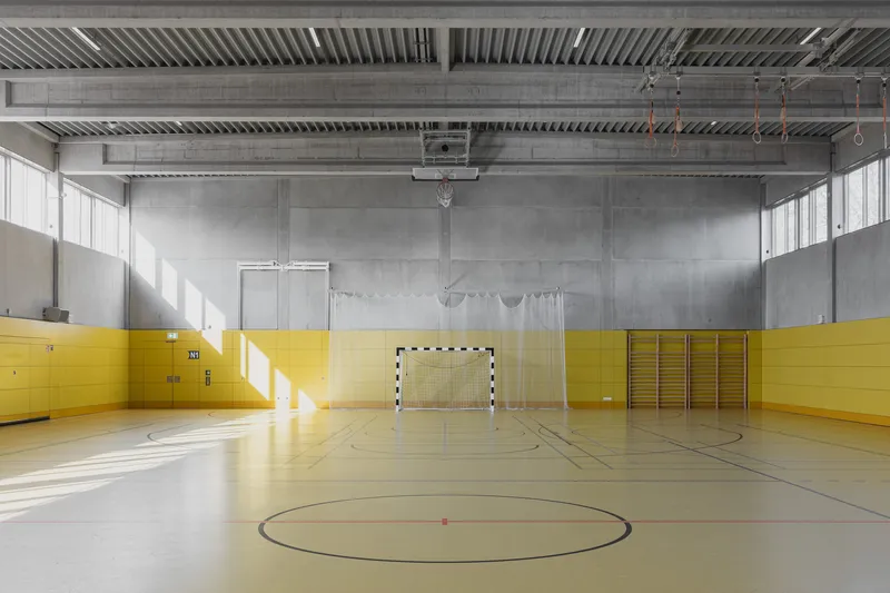 Gymnasium with yellow wall padding and exposed steel ceiling beams with sunlight streaming through high windows