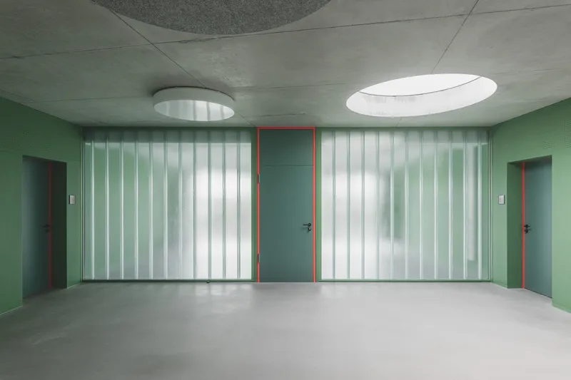 Corridor with translucent vertical glass panels flanking doors painted in green and red under oval skylights