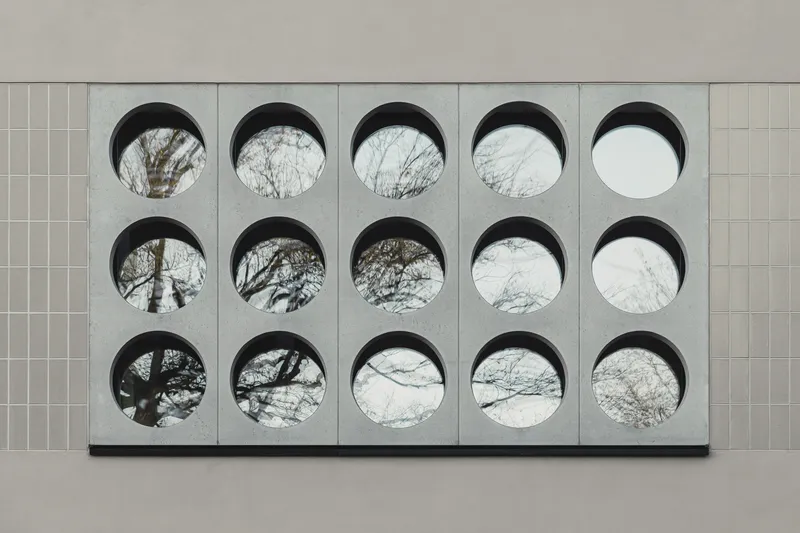 Close-up of fifteen circular openings in concrete panel framing views of bare tree branches