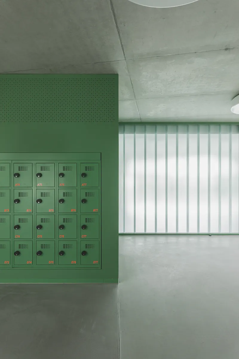 Interior hallway with green metal locker bank, exposed concrete ceiling, and vertical translucent wall panels