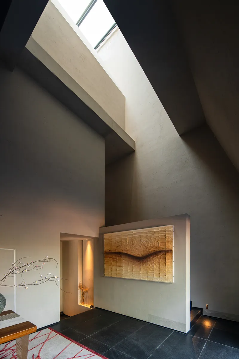 Double-height entry hall with linear skylight above timber-wrapped fireplace surround and dark tile floor