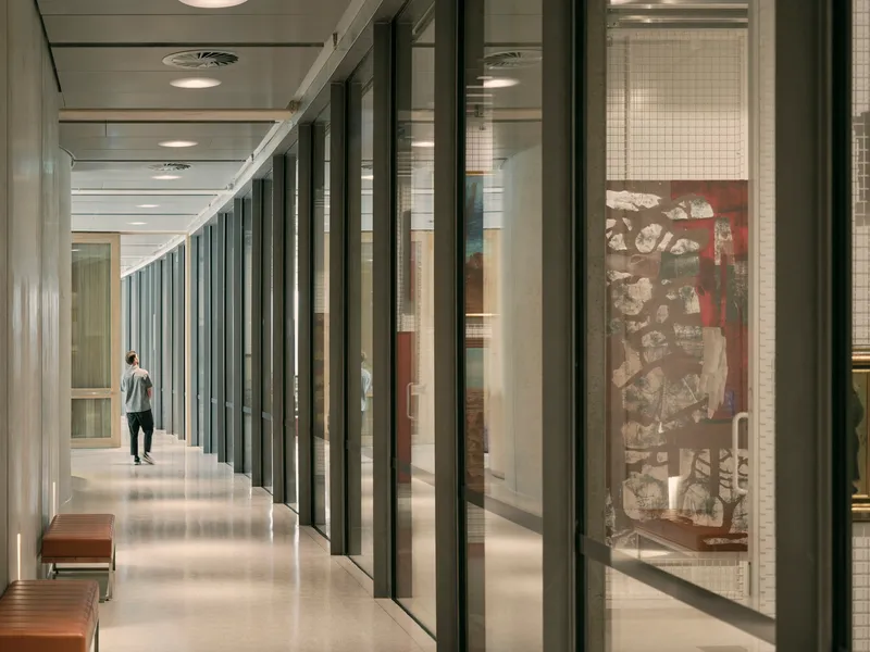 Corridor with floor-to-ceiling glass walls and vertical metal fins with a single visitor walking through