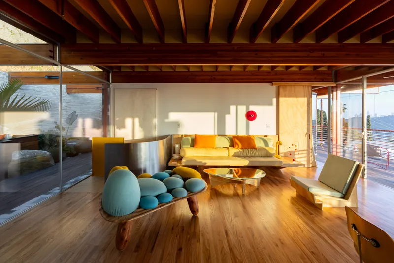 Living room with exposed timber beam ceiling and floor-to-ceiling glass walls framing afternoon sunlight