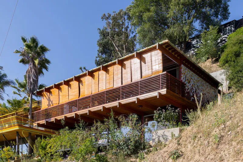 Hillside elevation showing cantilevered timber volume with horizontal slat railing and native trees