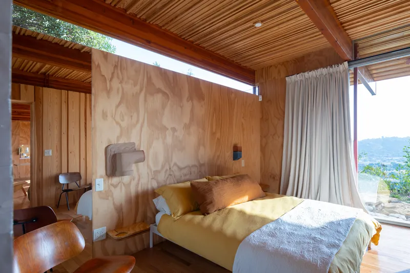 Bedroom with plywood headboard wall and clerestory window casting natural light onto the bed