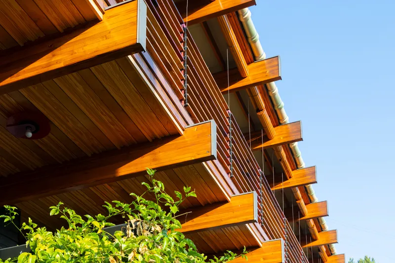 Upward view of stacked timber balconies with horizontal slat railings beneath a clear blue sky
