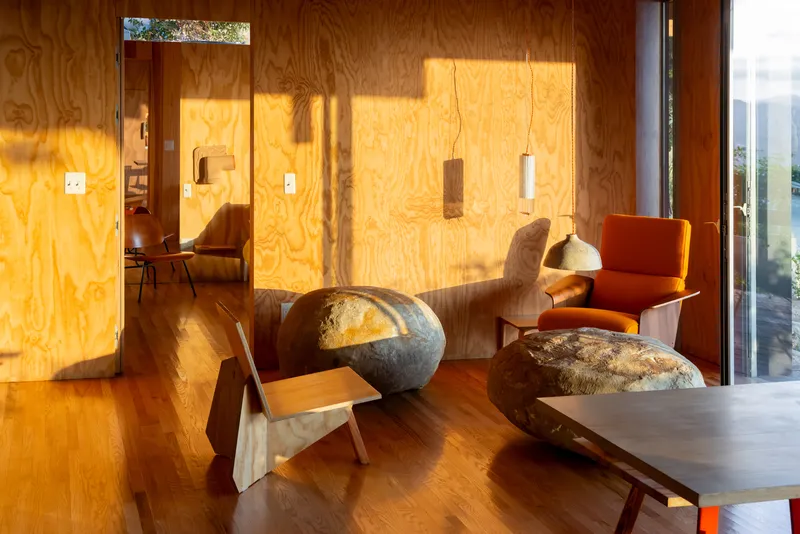 Living area with plywood paneled walls lit by afternoon sunlight streaming through clerestory windows