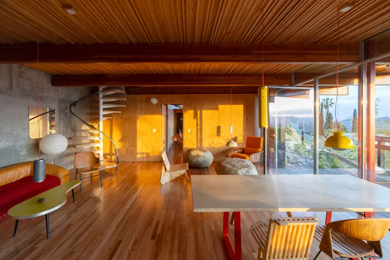 Open plan interior with exposed timber beams and full-height glazing overlooking hillside landscape at dusk