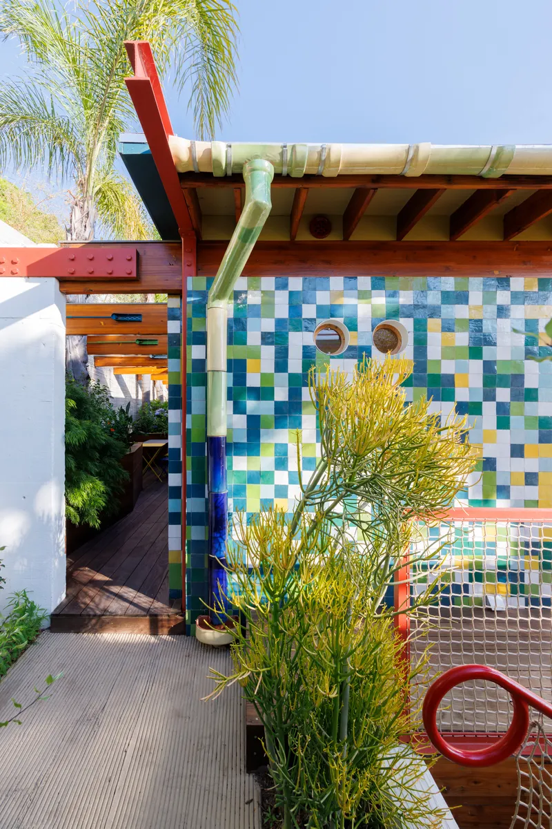 Exterior courtyard with multicolored mosaic tile wall and exposed timber roof beams with palm fronds
