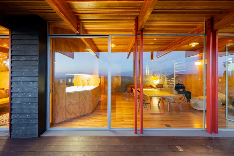 Glass facade at dusk showing dining area with timber ceiling and a person seated inside