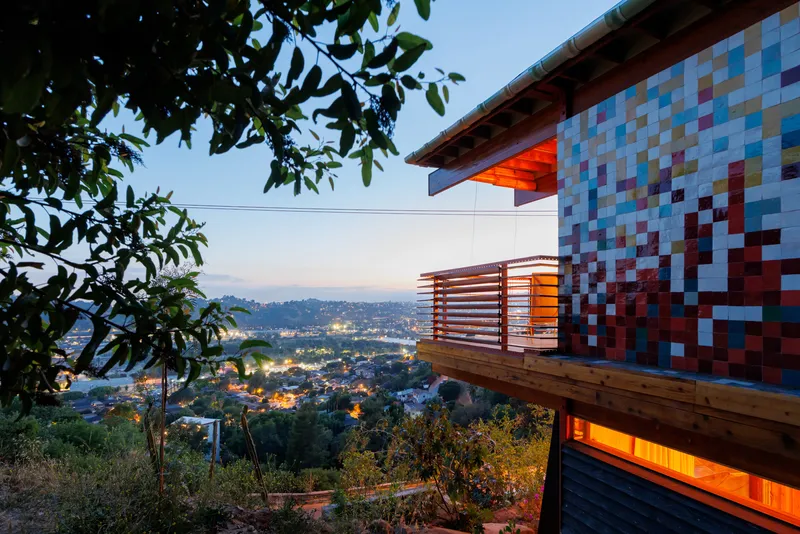 Cantilevered timber balcony with horizontal slat railing and mosaic tile wall at twilight