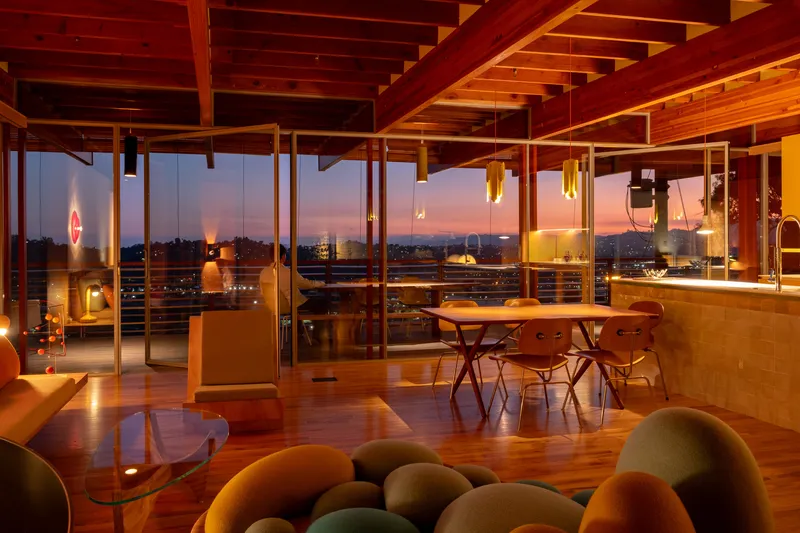 Interior view through glass walls toward city lights at dusk with timber ceiling above