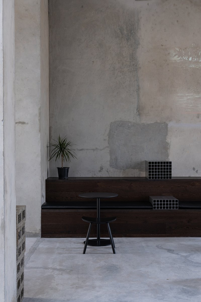 Dark timber bench against patched concrete wall with a small potted plant and metal stool