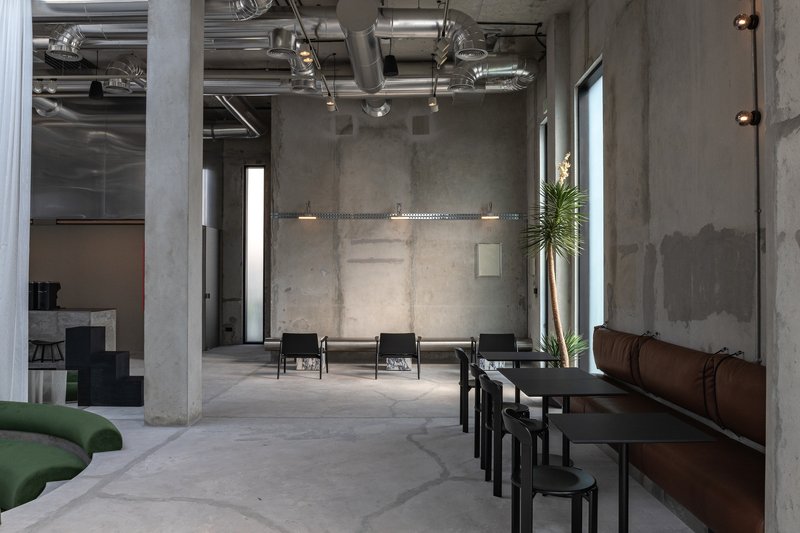 Row of low tables and stools along leather banquette seating with tall plant beside window
