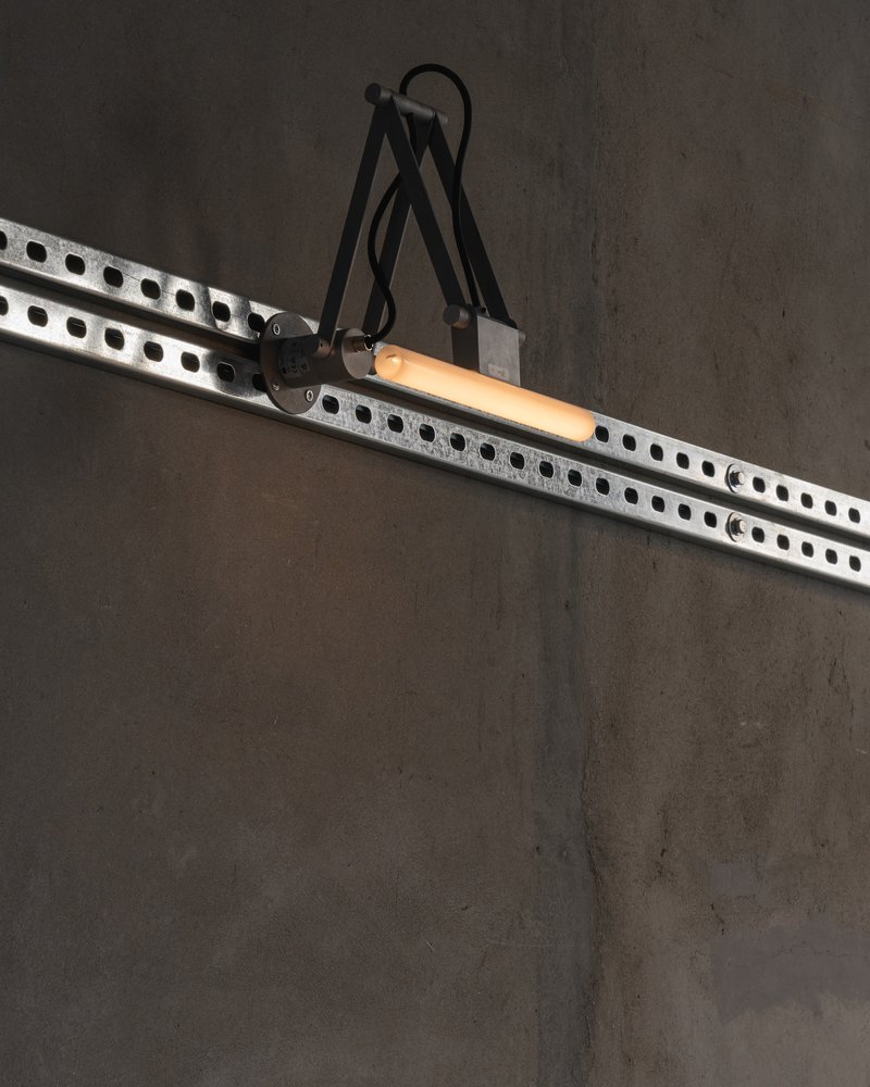 Articulated task light mounted on a perforated steel track against a grey wall