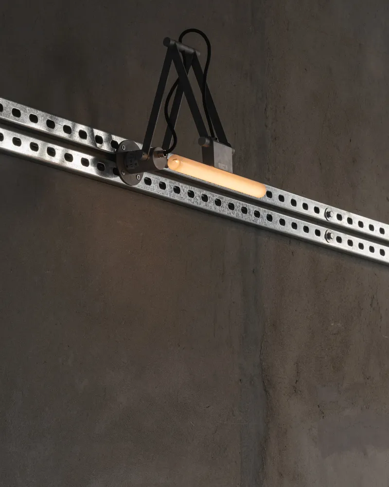 Articulated task light mounted on a perforated steel track against a grey wall