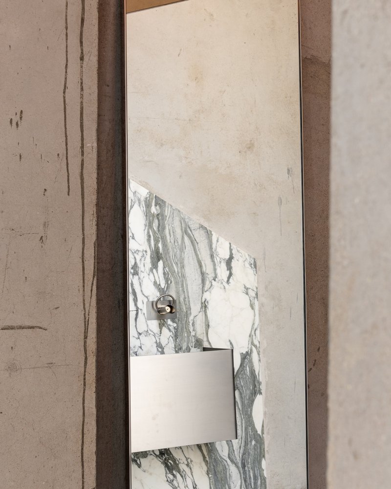 Detail of a marbled stone panel with white switch plate and bronze fixture against a plastered wall