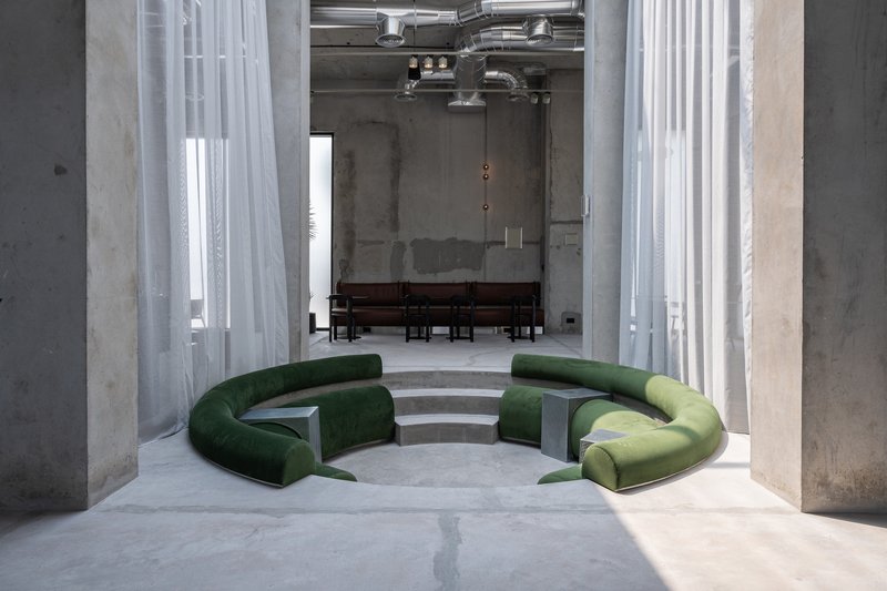 Sunken circular seating pit with green upholstered benches between white sheer curtains