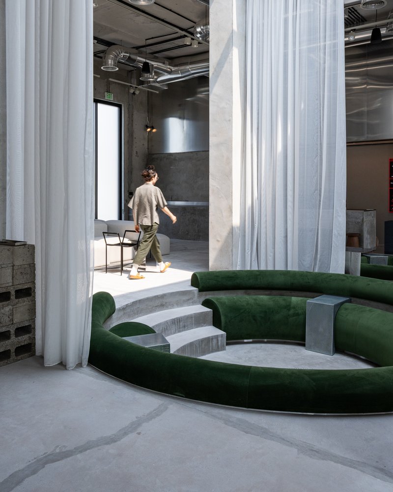 Figure walking past stepped concrete seating and white fabric partitions in afternoon light