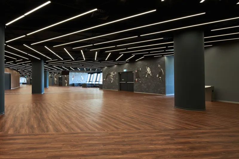 Interior lobby space with herringbone wood flooring and linear ceiling lights over dark columns and walls
