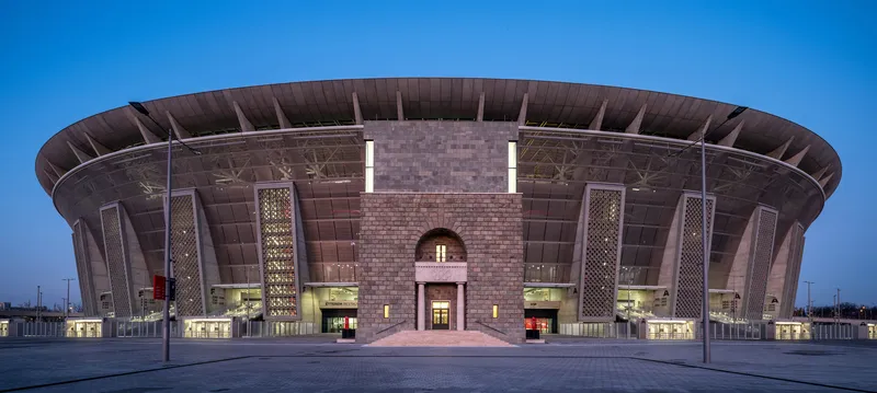 Arched entrance portal flanked by latticed towers and horizontal glazing at twilight