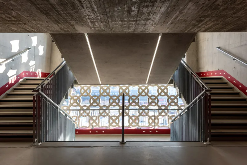 Symmetrical staircase with concrete soffit and patterned screens under linear ceiling lights