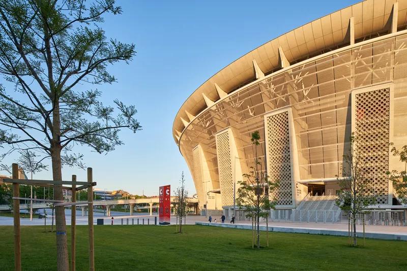 Plaza with young trees facing the curved facade and lattice screens in warm afternoon light