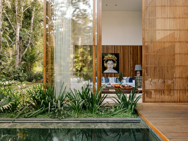 View across reflecting pool with timber deck and planted bed framing a glass-walled living room