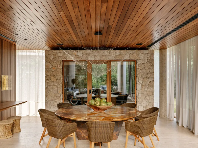 View of the dining table through timber-framed openings in the stone wall under a slatted ceiling