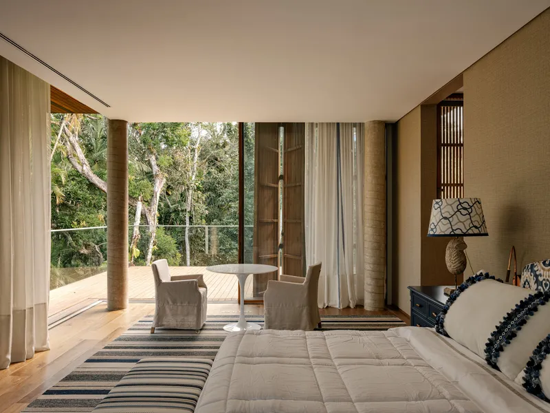 Bedroom opening to timber deck terrace framed by floor-to-ceiling glass and trees beyond