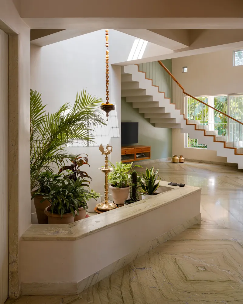 Entry foyer with floating staircase, vertical metal balustrade, and potted plants beneath a suspended brass lamp