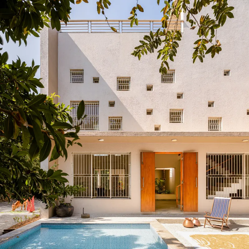 White stucco courtyard facade with scattered square windows and barred openings framing a small pool