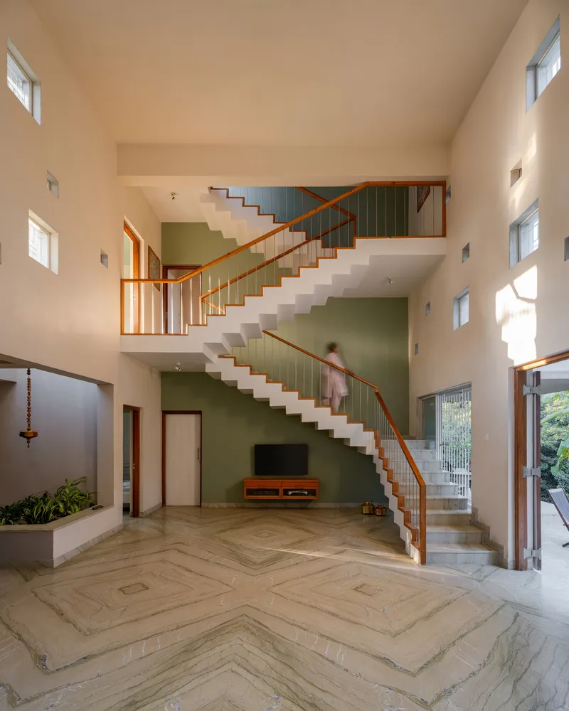 Open staircase with timber handrails ascending across a green accent wall in the main living space