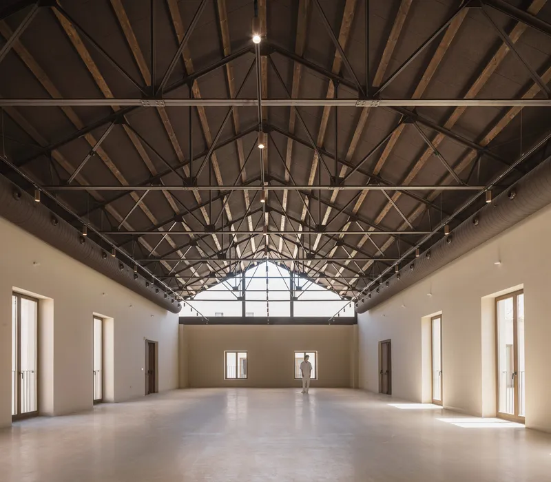 Interior hall with exposed timber truss roof structure and a single figure standing in the central bay
