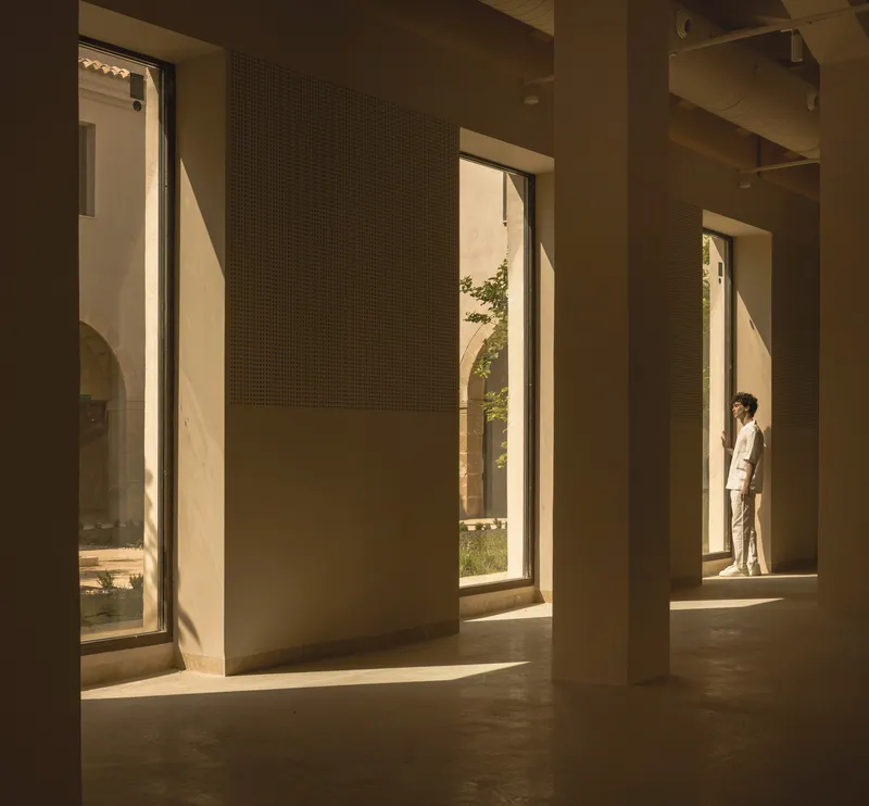 Sequence of tall openings with perforated panel walls and a figure in warm afternoon light