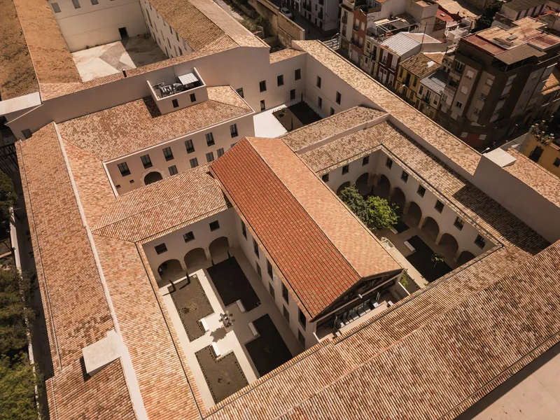 Aerial view of the terracotta-tiled roofs arranged around two interior courtyards in bright sunlight