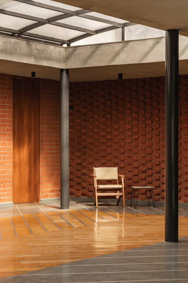 Slender steel columns supporting concrete beams and translucent roof panels above the terracotta-tiled courtyard floor