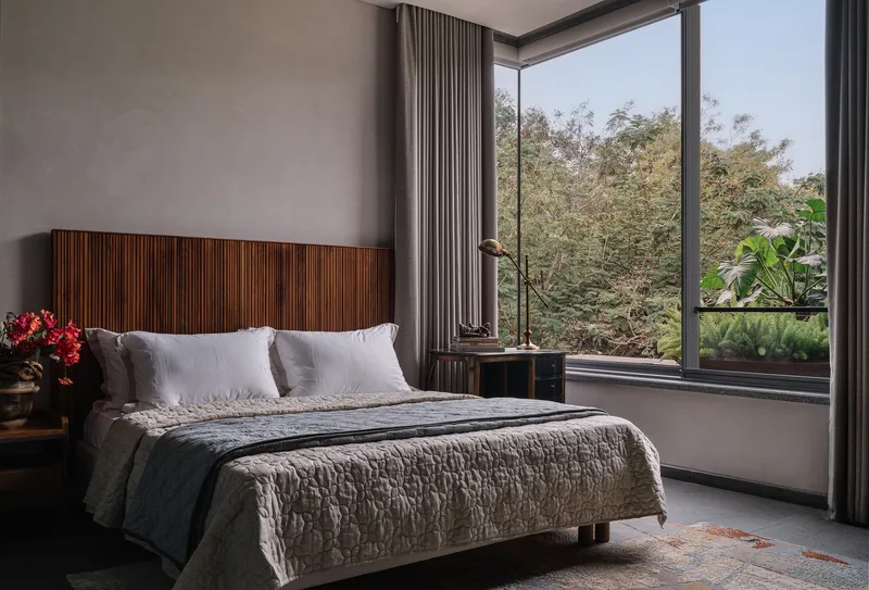 Bedroom with horizontal slat timber headboard and corner windows overlooking mature trees