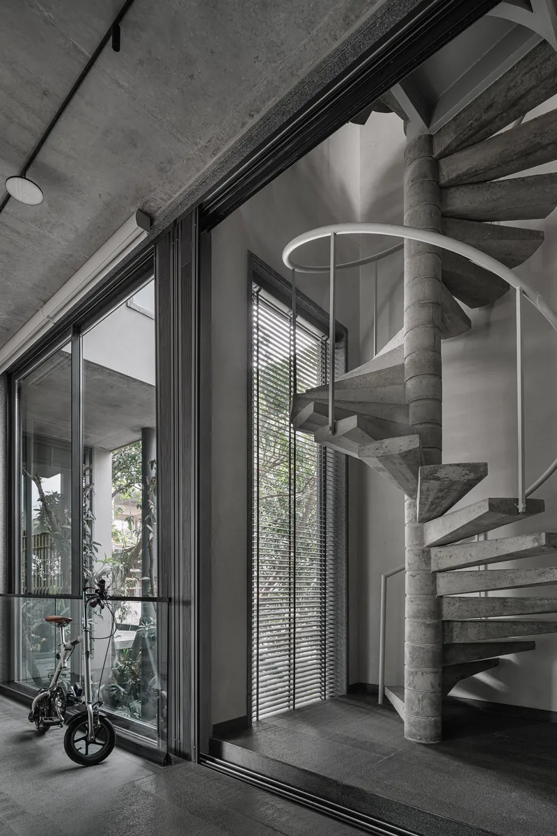 Helical concrete staircase with white metal railing beside floor-to-ceiling glazing and horizontal blinds