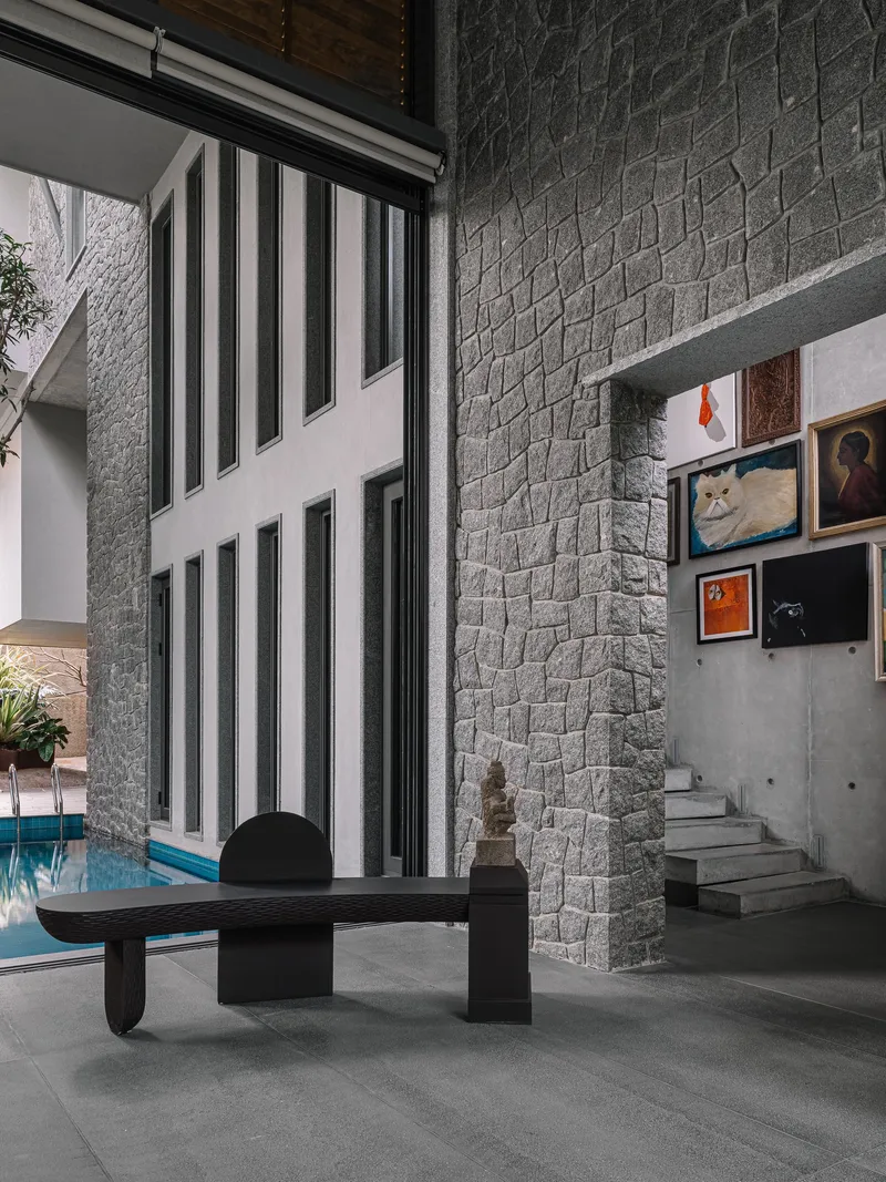 Interior courtyard with textured stone wall, concrete staircase, and floor-to-ceiling windows overlooking a pool