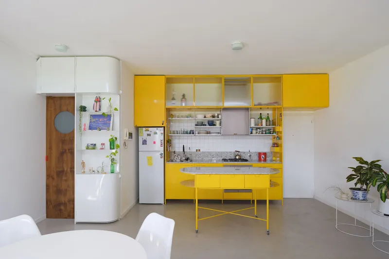 Yellow lacquered kitchen cabinetry with curved island and sliding glass doors beneath white upper units