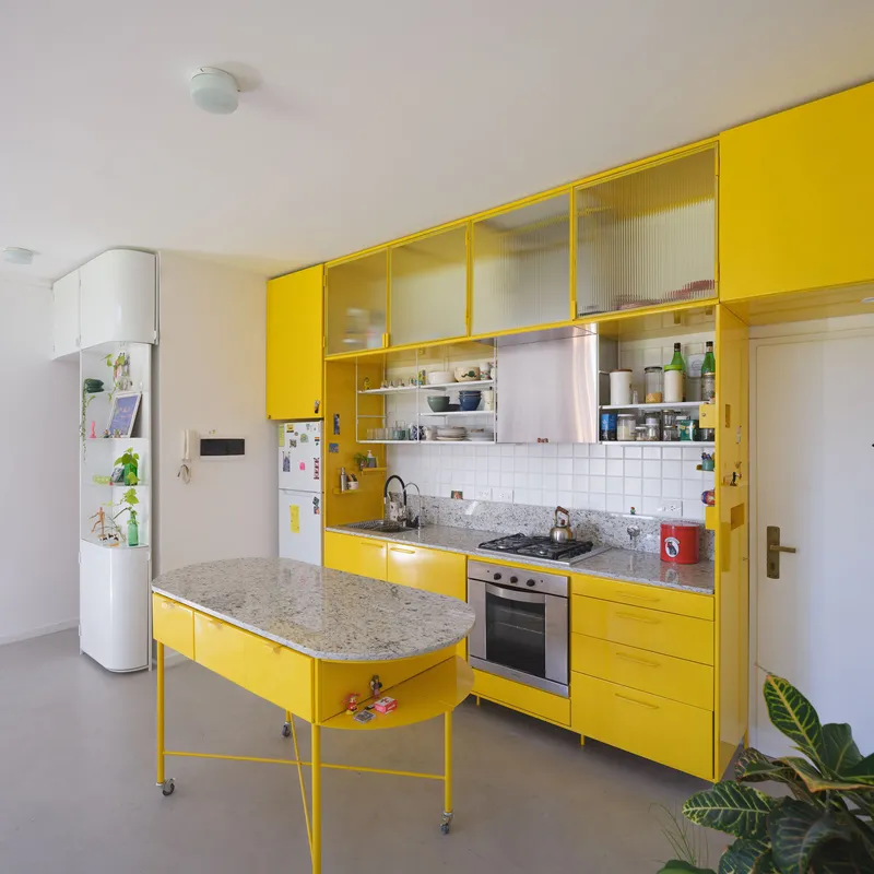 Kitchen island with terrazzo top on wheels beneath yellow cabinets with fluted glass sliding doors