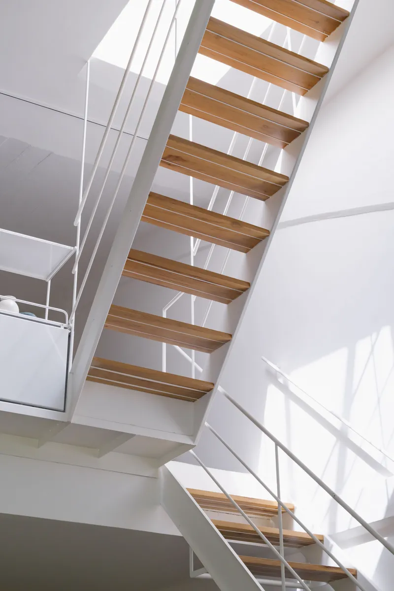 Open timber tread staircase with white steel cable railing in sunlit multi-story volume