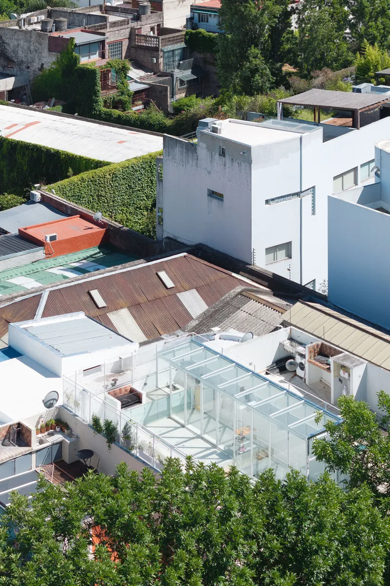 Aerial view of white rooftop terrace with glass enclosure and timber deck among neighboring houses
