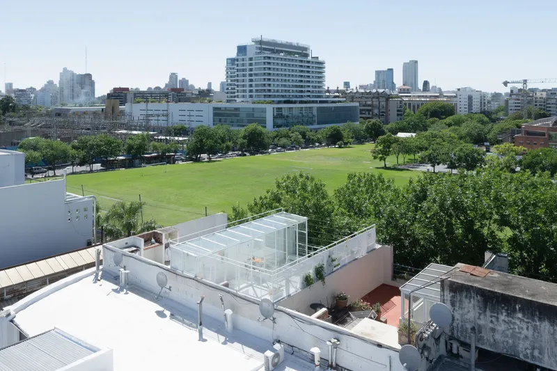 Rooftop glass pavilion overlooking a green park with trees and surrounding urban buildings