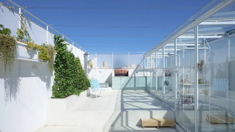 White terrace deck with glazed enclosure, green wall planting, and blue lounge chairs under midday sun