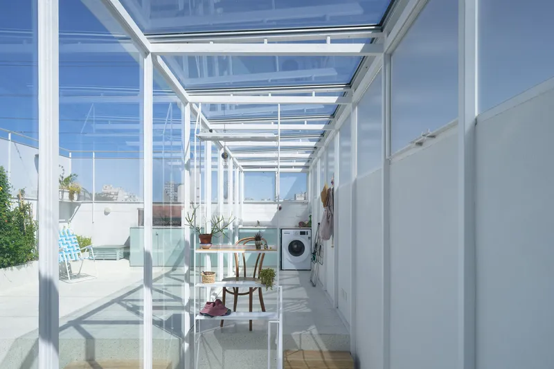 Glazed corridor with exposed white steel framing and laundry area visible inside transparent walls