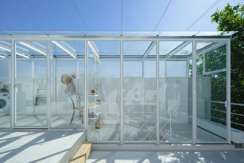 Glass and aluminum frame enclosure on a rooftop terrace with a wooden bench casting shadows in sunlight