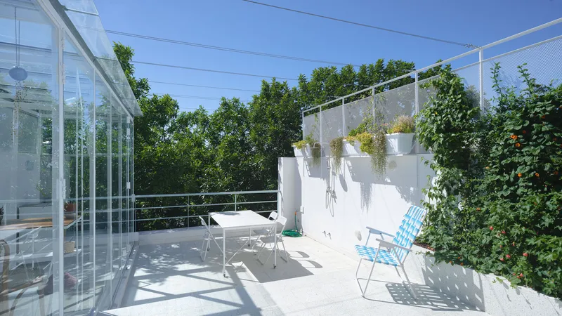 White planter wall with hanging plants next to a glass pavilion and wire mesh chairs on the terrace